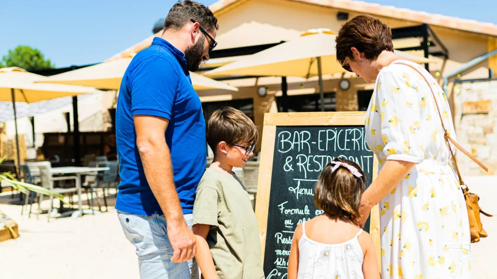 Famille devant le menu du Bistrot de Pays l"Auberge de Planzolles", en été