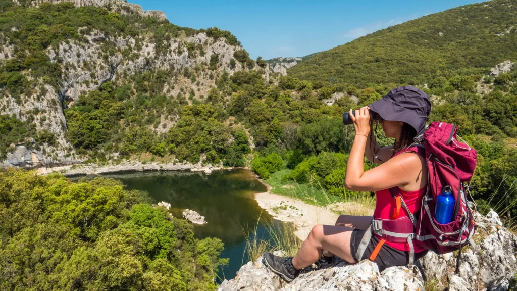 Woman observing the surroundings through binoculars during her hike in the Ardèche Gorges, in summer