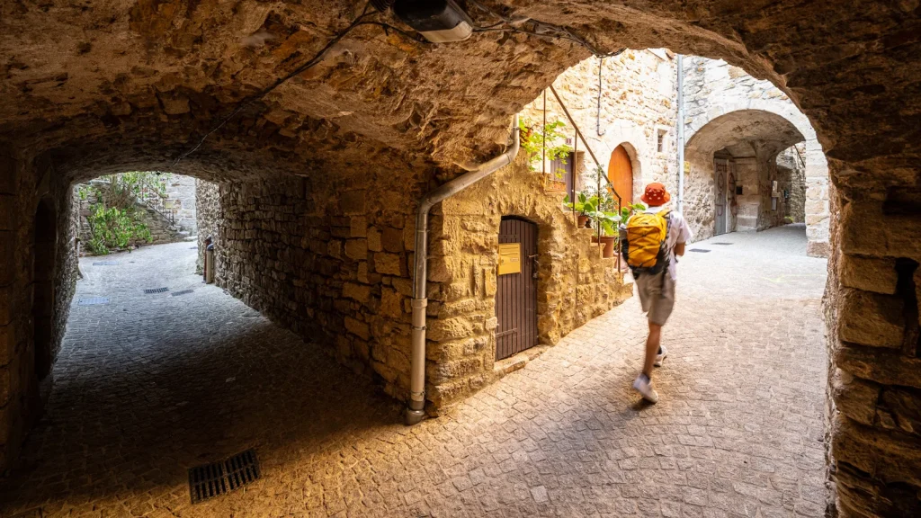 Homme déambulant dans les ruelles voutées du village de caractère de Vinezac, en été