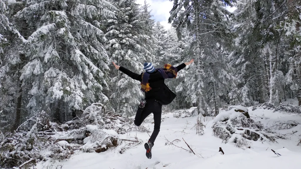 Personne sautant de joie dans un bois sous la neige, en hiver