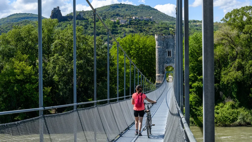 Woman with her bike, on the himalayan footbridge in the village with outstanding character of Rochemaure, in spring. Roaming, she will join the ViaRhôna