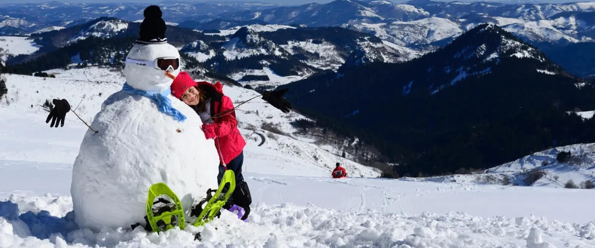 Fillette faisant un câlin à un bonhomme de neige en haut à la Croix de bauzon, en hiver