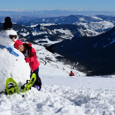 Fillette faisant un câlin à un bonhomme de neige en haut à la Croix de bauzon, en hiver