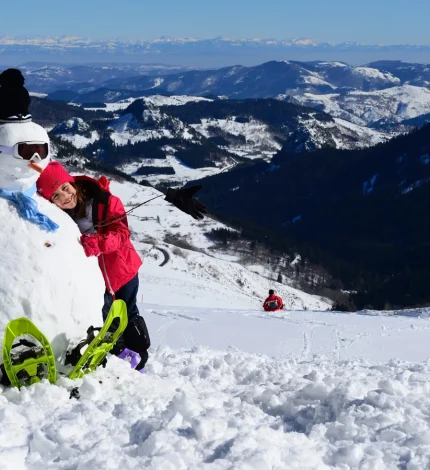 Fillette faisant un câlin à un bonhomme de neige en haut à la Croix de bauzon, en hiver