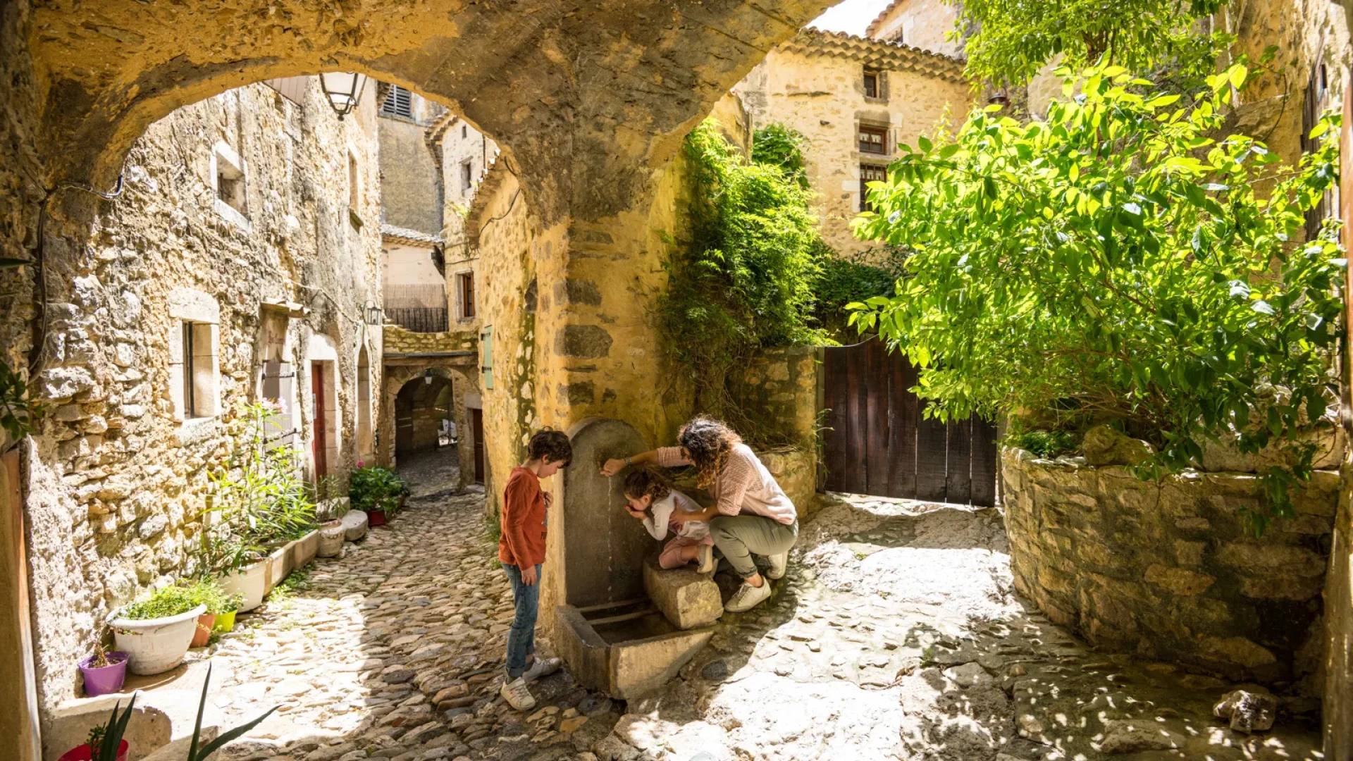 Famille se désaltérant à une fontaine dans le village de caractère de Saint-Montan, au printemps
