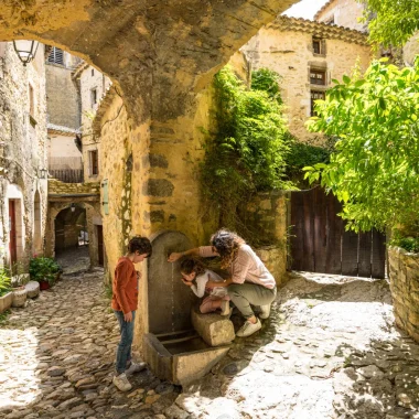 Famille se désaltérant à une fontaine dans le village de caractère de Saint-Montan, au printemps