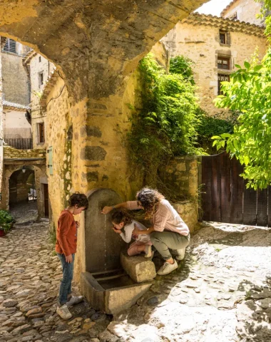 Famille se désaltérant à une fontaine dans le village de caractère de Saint-Montan, au printemps