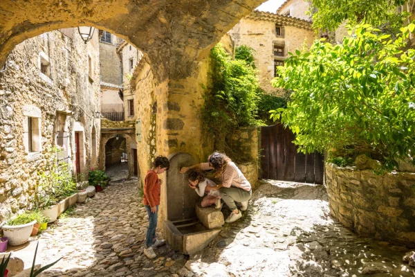 Famille se désaltérant à une fontaine dans le village de caractère de Saint-Montan, au printemps