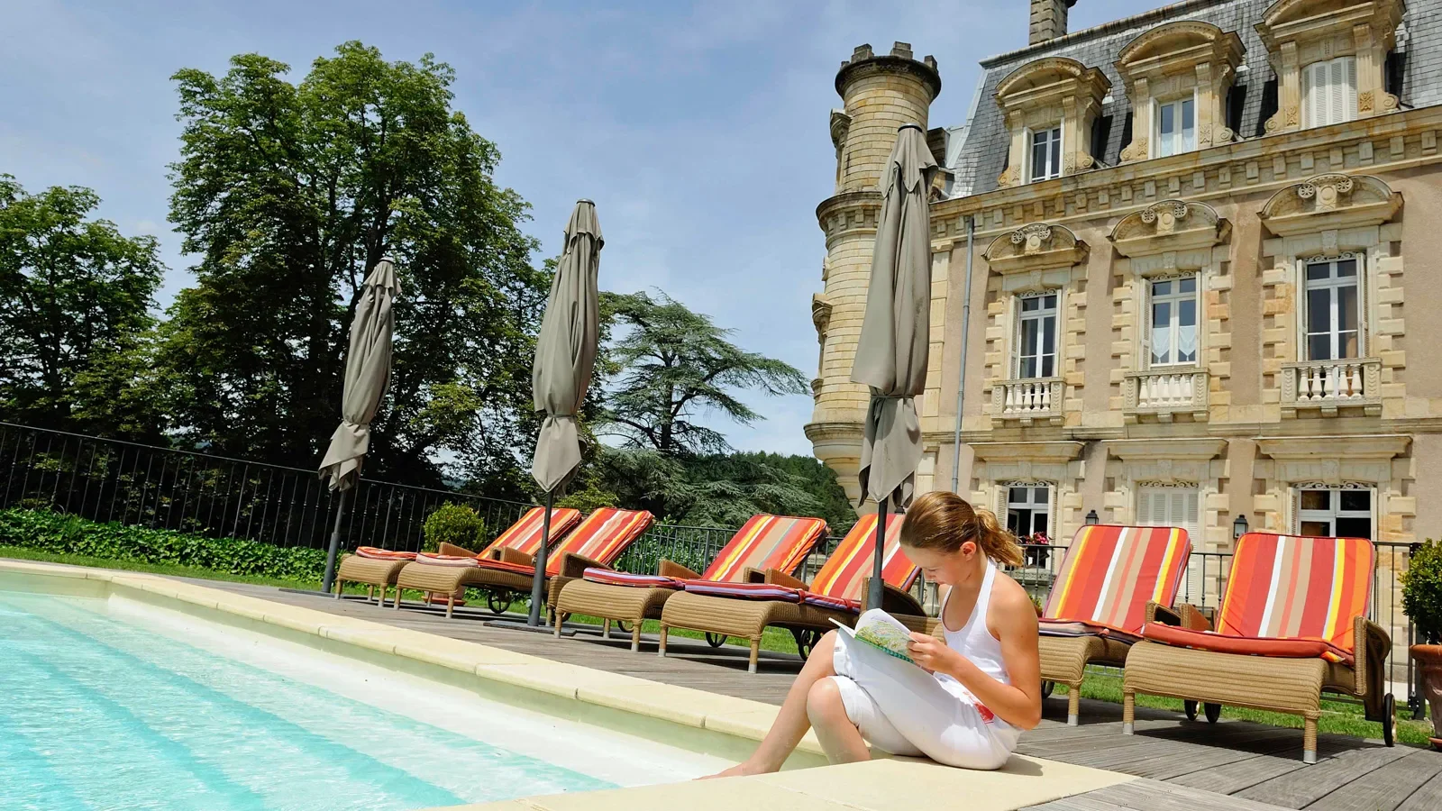 Petite fille lisant au bord de la piscine du Château Clément en été