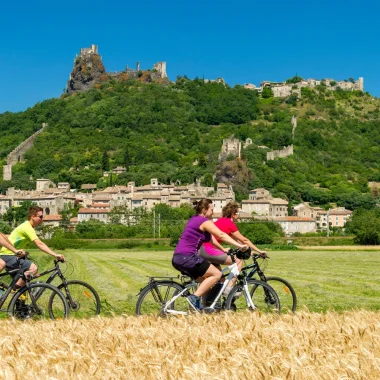Groupe d'amis roulant à vélo devant le village de caractère de Rochemaure, en été