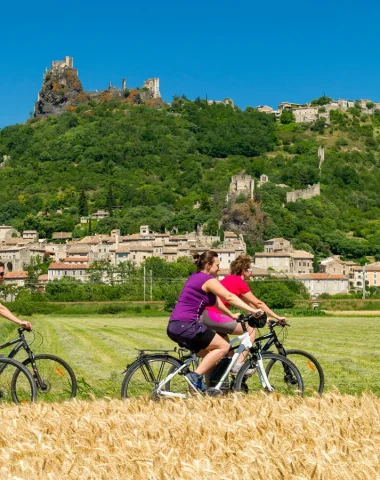 Groupe d'amis roulant à vélo devant le village de caractère de Rochemaure, en été