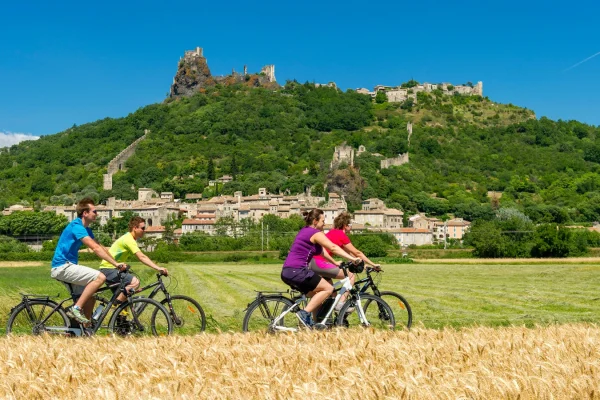 Groupe d'amis roulant à vélo devant le village de caractère de Rochemaure, en été