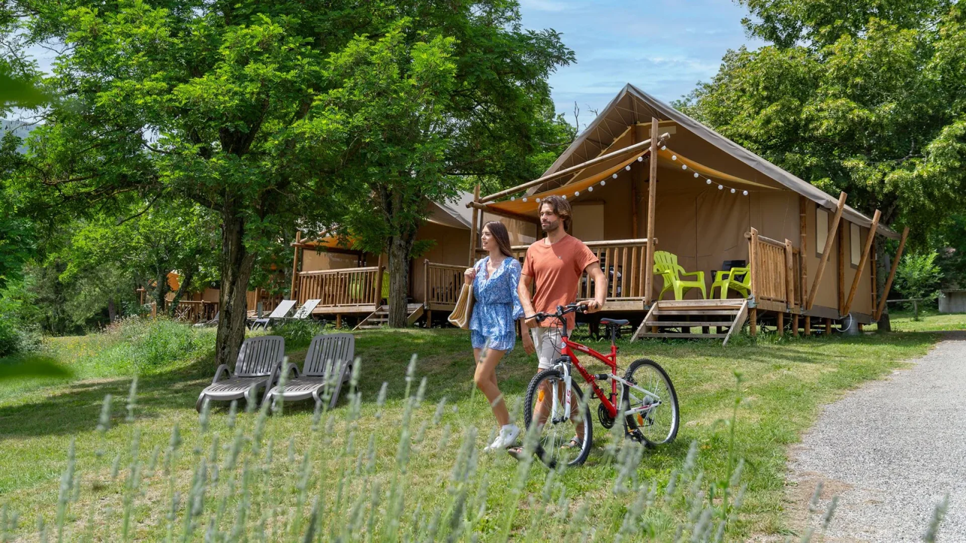 Couple partant en balade, avec un vélo, dans le camping "Les Jardins de Privas", en été
